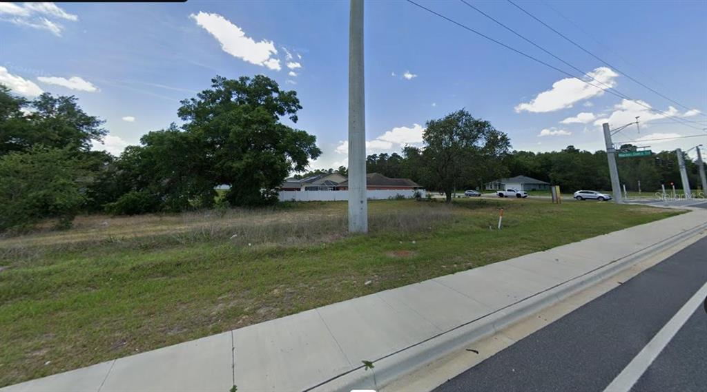 A vacant, grassy lot sits next to a sidewalk and a road with trees — LOT 9 SW 129TH PLACE, OCALA, FL