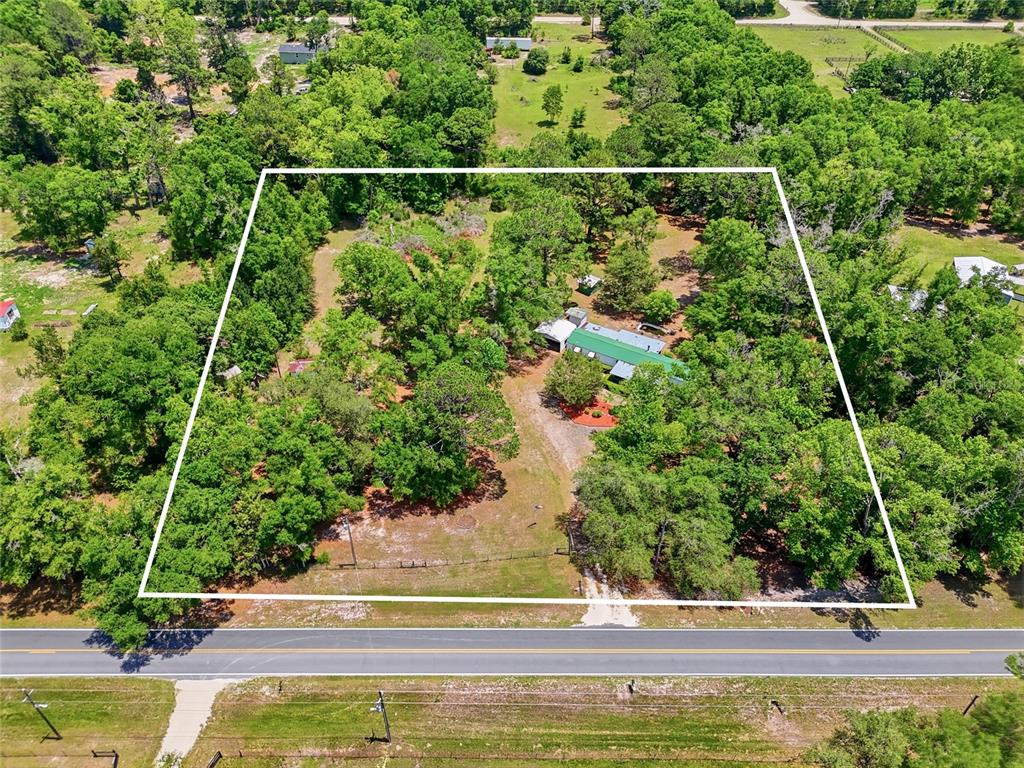 An aerial view shows a house with a green roof situated on a wooded lot — 20480 COUNTY ROAD 137, LAKE CITY, FL