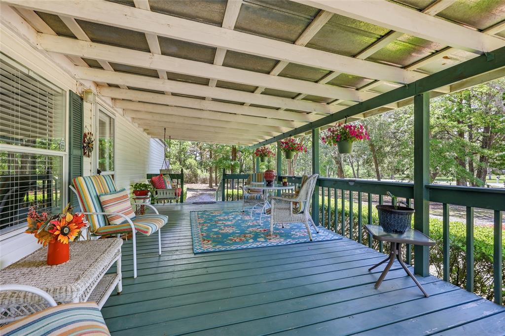 A covered wooden porch features outdoor seating, a floral rug, and hanging flower baskets — 20480 COUNTY ROAD 137, LAKE CITY, FL