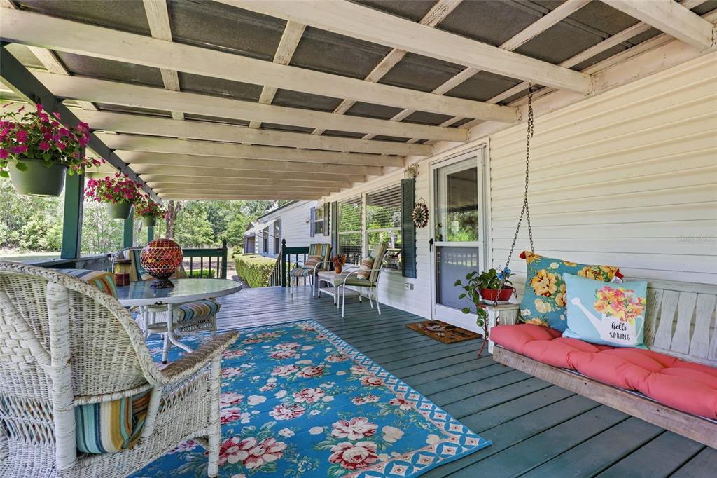 A covered porch features a hanging bench, wicker furniture, a floral rug, and potted flowers — 20480 COUNTY ROAD 137, LAKE CITY, FL