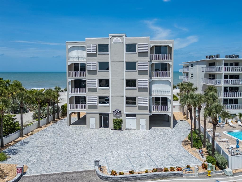 An exterior view of a multi-story beachfront condominium building with a paved parking lot — 19600 GULF BOULEVARD UNIT 102, INDIAN SHORES, FL