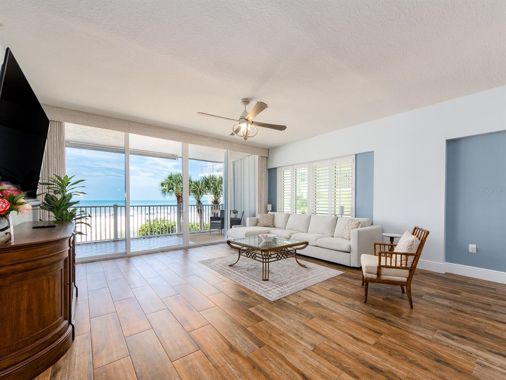 A living room features wood-look tile floors, a white sectional sofa, and a balcony view — 19600 GULF BOULEVARD UNIT 102, INDIAN SHORES, FL