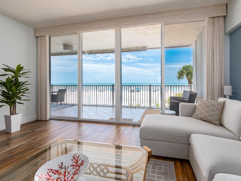 A living room with wood-look tile floors features a large sliding glass door overlooking the beach — 19600 GULF BOULEVARD UNIT 102, INDIAN SHORES, FL
