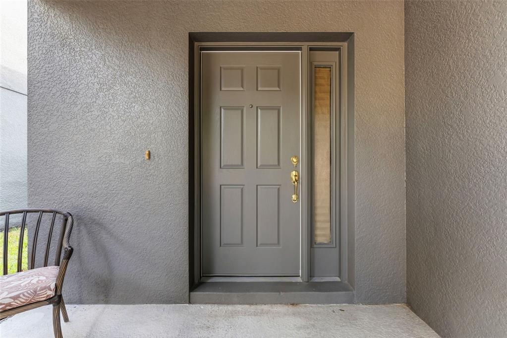 A gray front door with a side window and a chair on a concrete porch — 10257 NEWMINSTER LOOP, RUSKIN, FL