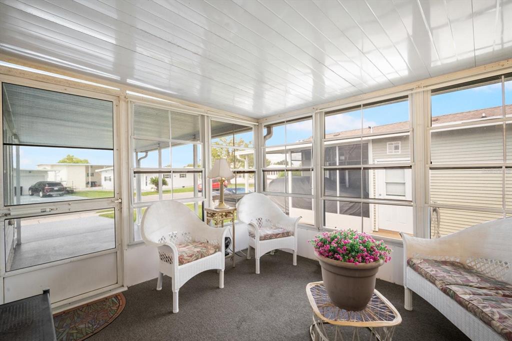 A sunroom with white wicker furniture, a potted plant, and large windows overlooking a neighborhood — 35045 CYNTHIA AVENUE, ZEPHYRHILLS, FL