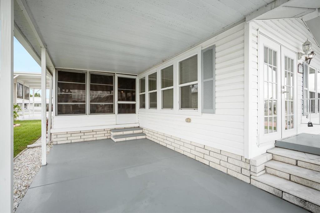A covered concrete patio features white siding, a screened-in section, and steps leading to a doorway — 35045 CYNTHIA AVENUE, ZEPHYRHILLS, FL
