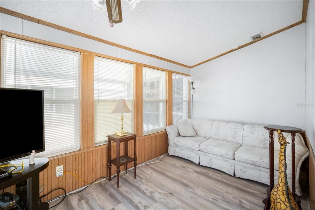 A living room features wood-paneled walls, light wood-look flooring, a white sofa, and large windows — 35045 CYNTHIA AVENUE, ZEPHYRHILLS, FL