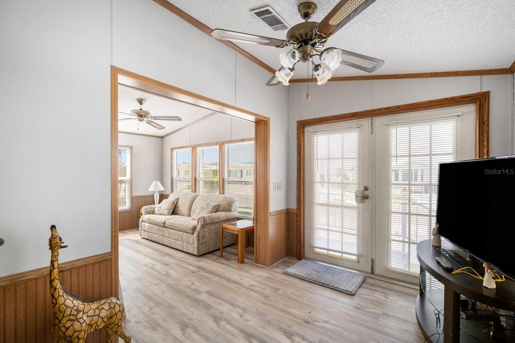 A living room with light wood-look flooring, a ceiling fan, and a view into a sunroom — 35045 CYNTHIA AVENUE, ZEPHYRHILLS, FL