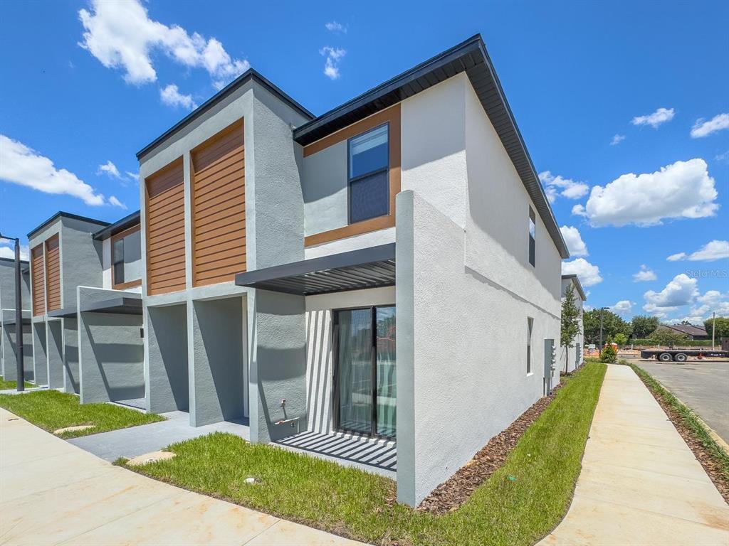 A modern two-story townhouse exterior features gray stucco walls, wood-look siding, and a metal pergola — 3229 ENERGY DRIVE, KISSIMMEE, FL