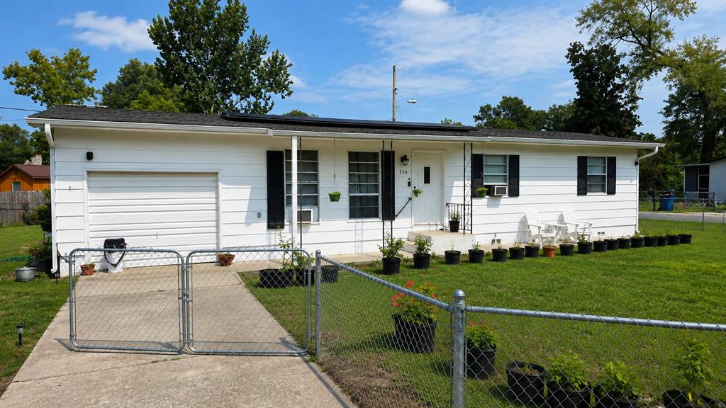 A single-story white house with a garage, a chain-link fence, and many potted plants — 354 PARK DRIVE, DELAND, FL