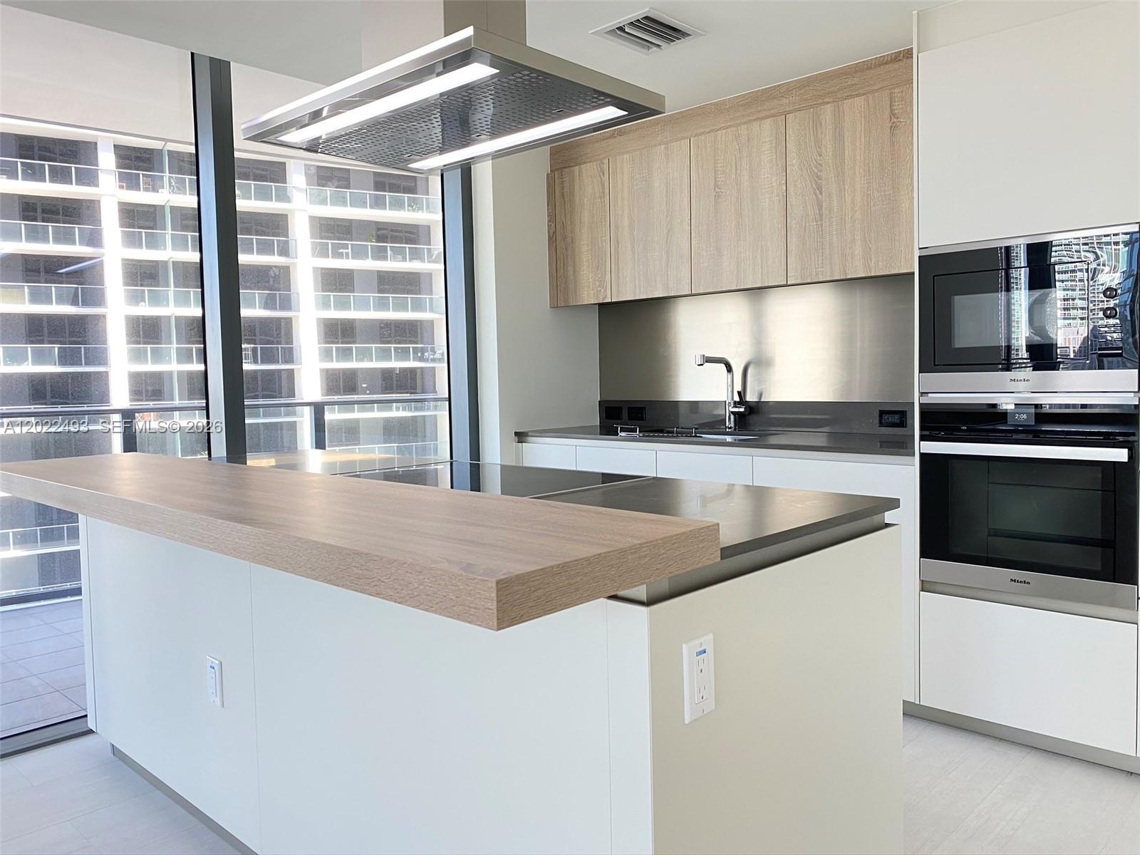 A modern kitchen features a wooden breakfast bar, white cabinetry, and stainless steel appliances — 1000 Brickell Plz # 2715, Miami FL 33131, MIAMI, FL