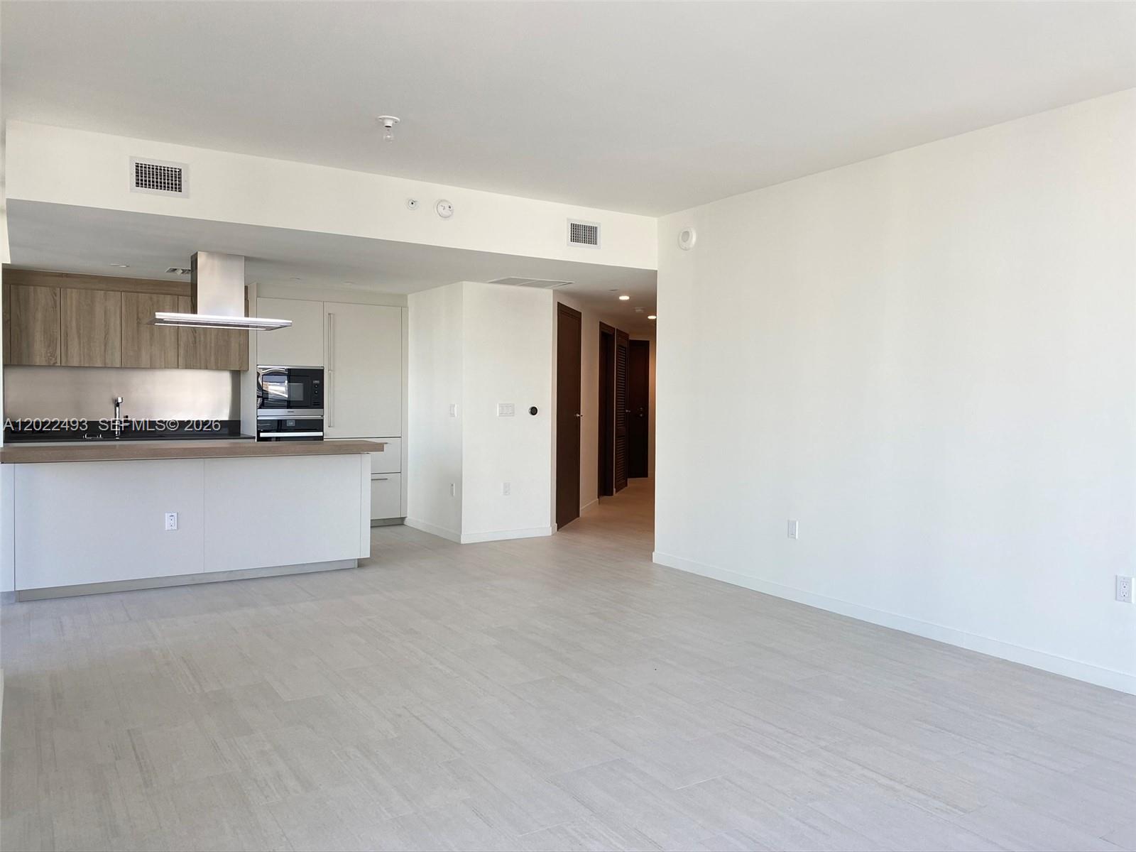 An open-concept living area features a modern kitchen with wood cabinets and a breakfast bar — 1000 Brickell Plz # 2715, Miami FL 33131, MIAMI, FL