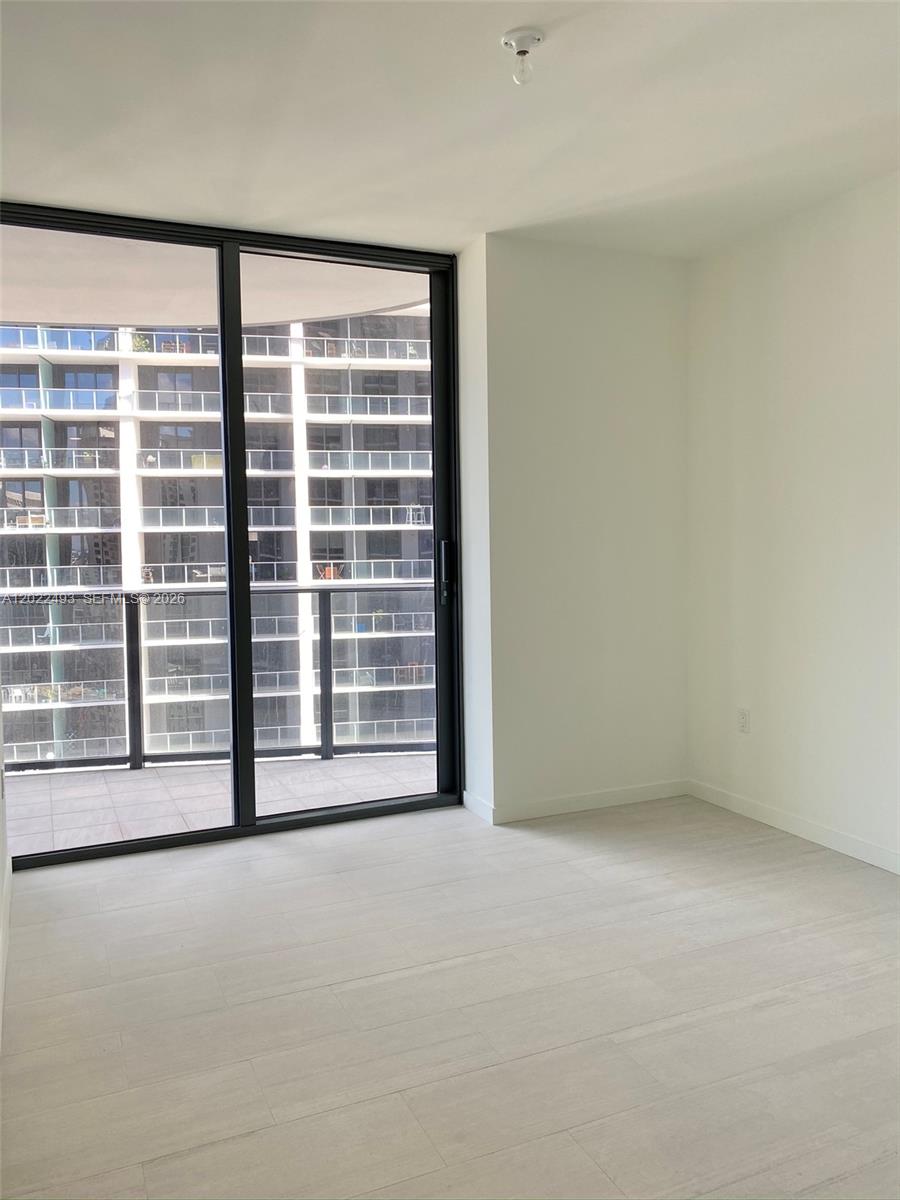 An empty room features light wood-look flooring, white walls, and a sliding glass door to a balcony — 1000 Brickell Plz # 2715, Miami FL 33131, MIAMI, FL