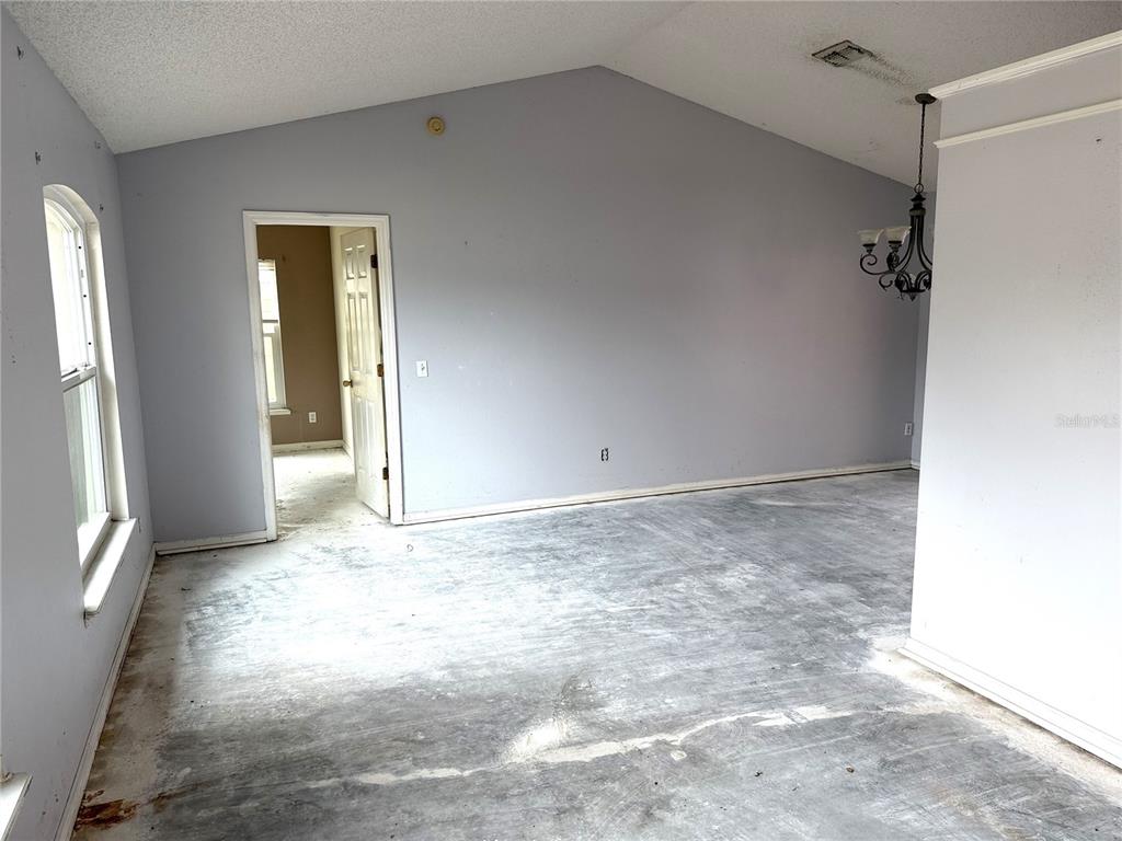 An empty room with gray walls, a vaulted ceiling, and an exposed concrete subfloor — 3208 KINGS RIDGE TERRACE, DELTONA, FL