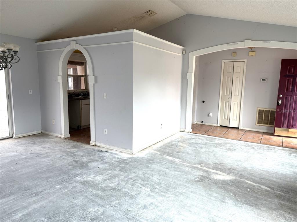 An interior view shows a living area with concrete floors, arched doorways, and a kitchen pass-through — 3208 KINGS RIDGE TERRACE, DELTONA, FL