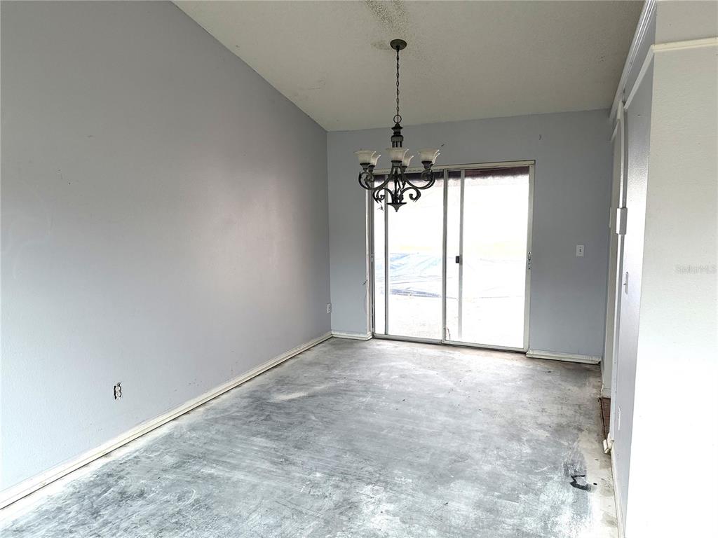 An empty dining room features light gray walls, a chandelier, and an unfinished concrete floor — 3208 KINGS RIDGE TERRACE, DELTONA, FL