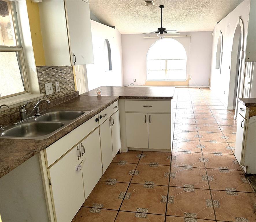 A kitchen with white cabinets, laminate countertops, and tiled floors overlooks an adjacent living area — 3208 KINGS RIDGE TERRACE, DELTONA, FL