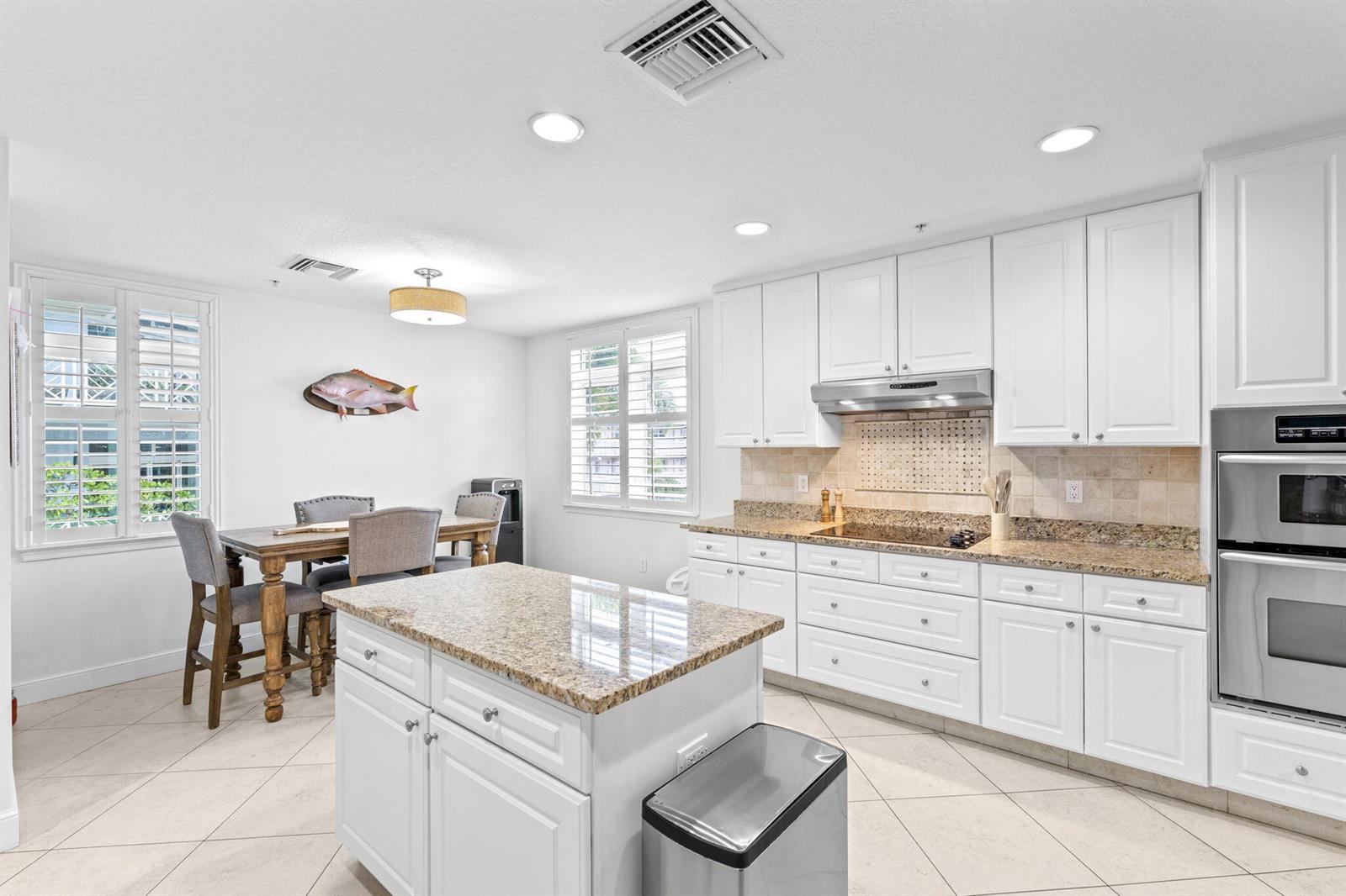 A kitchen with white cabinets, granite countertops, a center island, and an adjacent dining area — 305 E Ocean Avenue # 7, Lantana FL 33462, LANTANA, FL