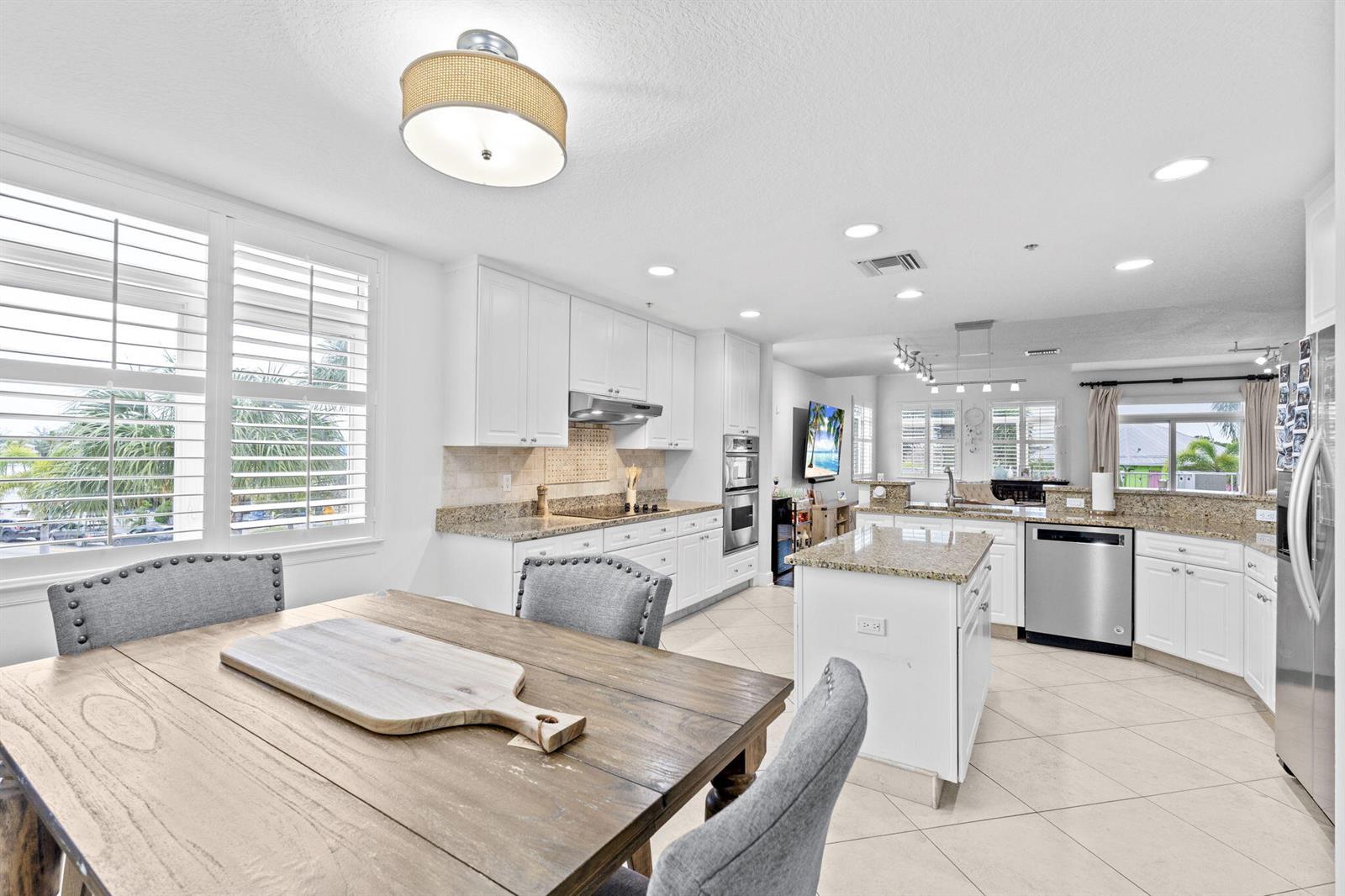 A kitchen with white cabinets, granite countertops, and an island opens to a dining area — 305 E Ocean Avenue # 7, Lantana FL 33462, LANTANA, FL
