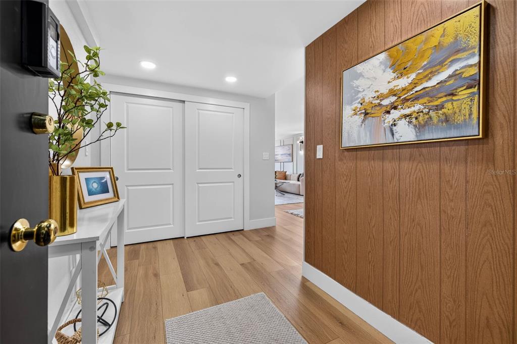 An entryway features wood-paneled walls, light wood flooring, white sliding doors, and a console table — 100 OAKMONT LANE UNIT 204, BELLEAIR, FL