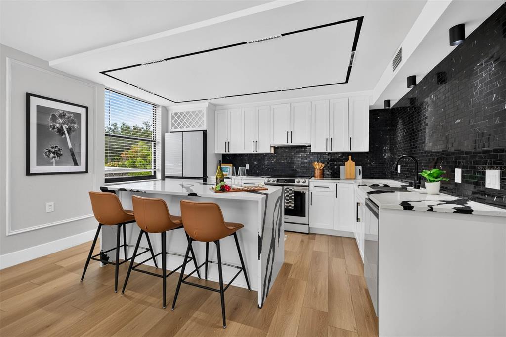 A modern kitchen features white cabinets, black tile backsplashes, and a marble-topped island with stools — 100 OAKMONT LANE UNIT 204, BELLEAIR, FL