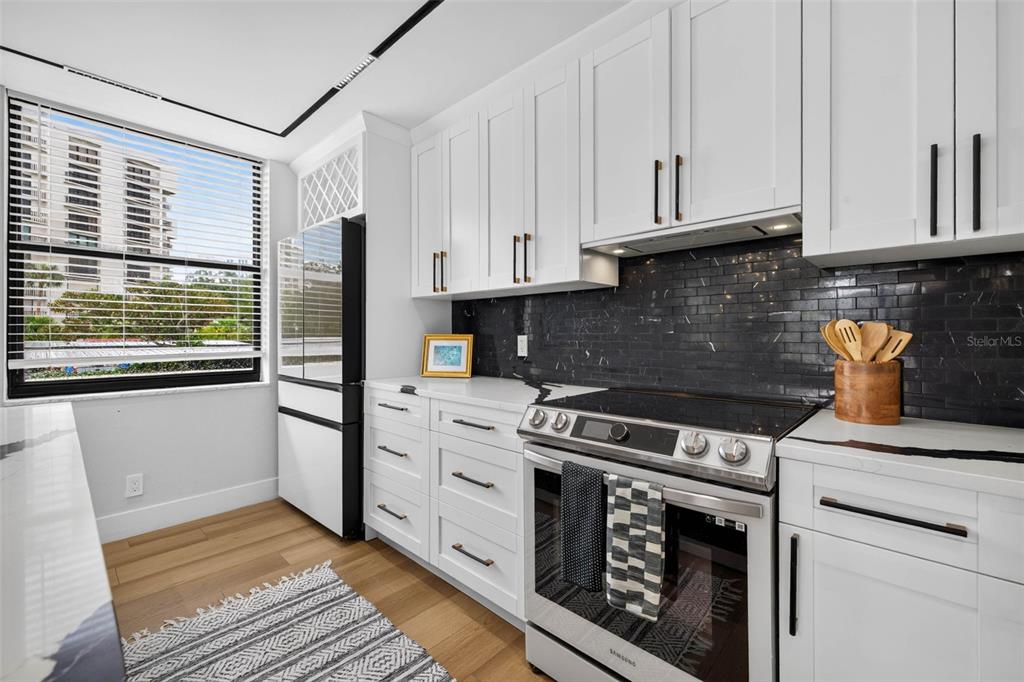 A modern kitchen features white cabinets, a black tiled backsplash, stainless steel appliances, and wood floors — 100 OAKMONT LANE UNIT 204, BELLEAIR, FL