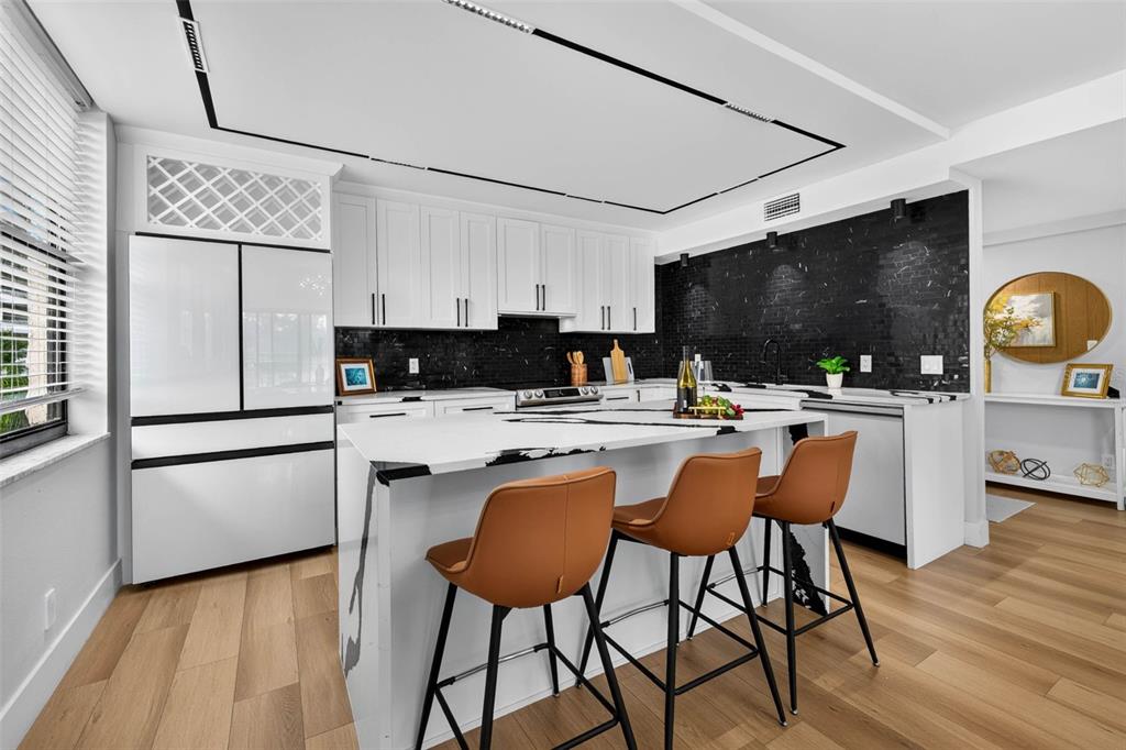 A modern kitchen features white cabinetry, a black tile backsplash, and a white waterfall island — 100 OAKMONT LANE UNIT 204, BELLEAIR, FL