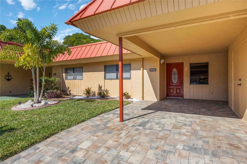 A tan house exterior features a red metal roof, paved entryway, and a front door — 9608 VALENCIA COVE, BRADENTON, FL