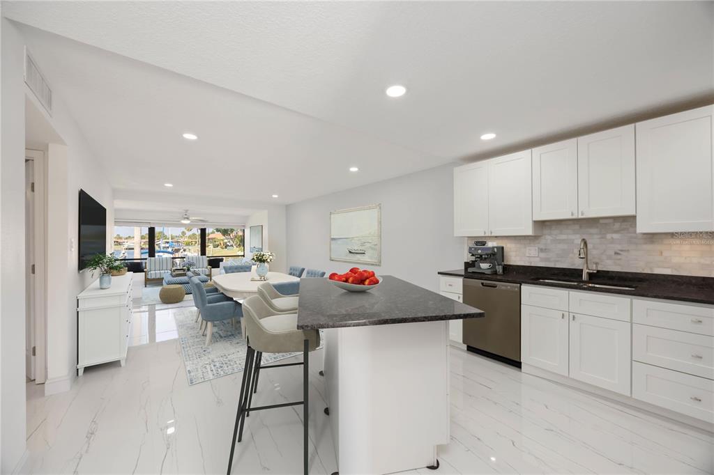 A modern kitchen with white cabinets and a dark island overlooks a dining area — 9608 VALENCIA COVE, BRADENTON, FL