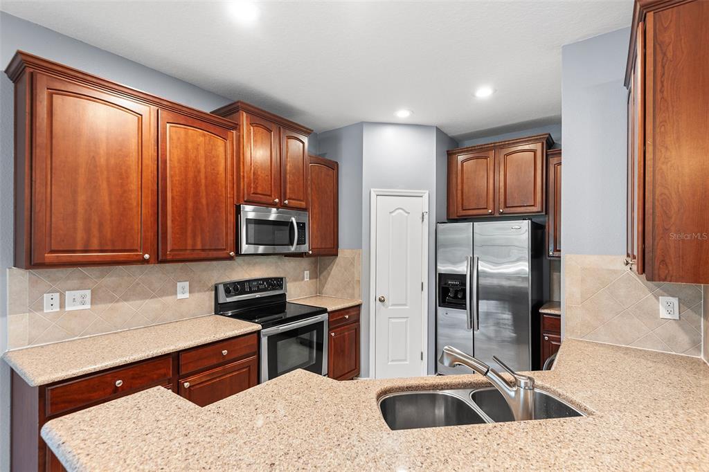 A kitchen features cherry wood cabinets, granite countertops, stainless steel appliances, and a double sink — 6745 BREEZY PALM DRIVE, RIVERVIEW, FL