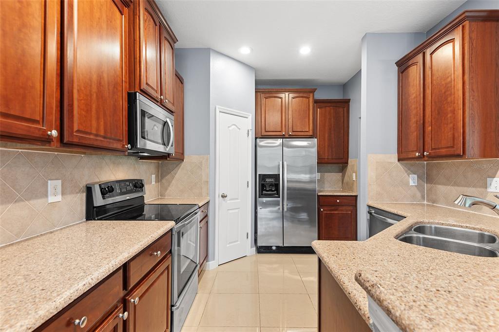 A kitchen features wood cabinets, stainless steel appliances, granite countertops, and light tile flooring — 6745 BREEZY PALM DRIVE, RIVERVIEW, FL