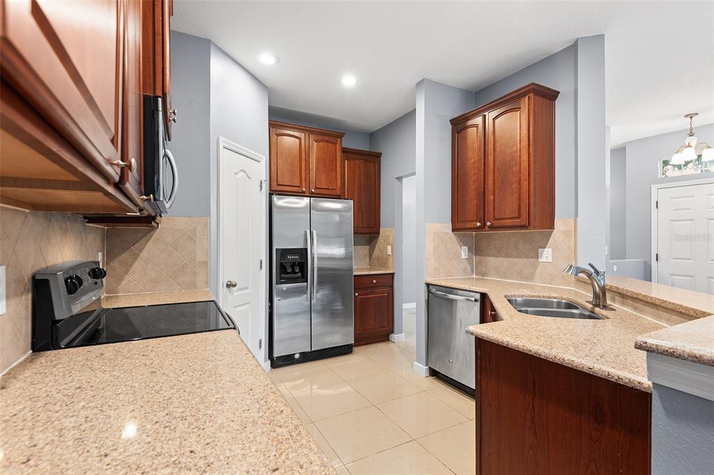 A kitchen features wood cabinets, granite countertops, stainless steel appliances, and light-colored tile flooring — 6745 BREEZY PALM DRIVE, RIVERVIEW, FL