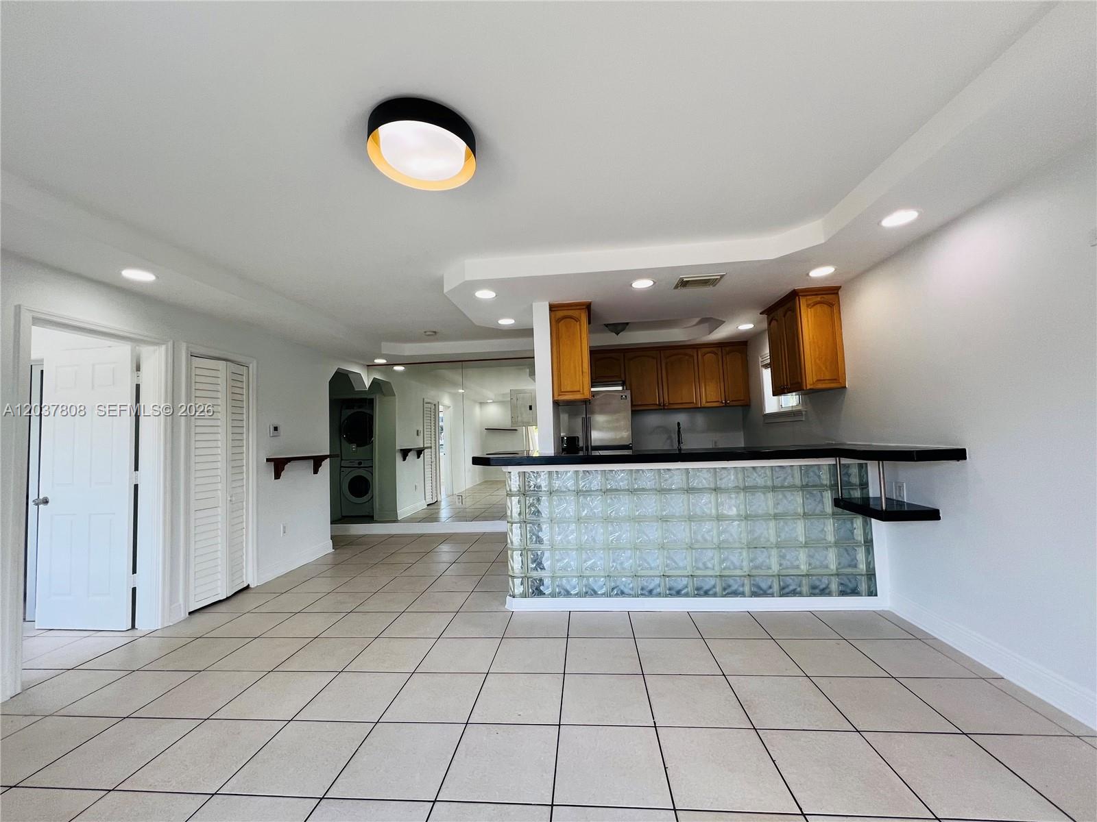 A kitchen features a glass block breakfast bar, wooden cabinets, and light-colored tile flooring — 2033 Calais Dr # 5, Miami Beach FL 33141, MIAMI BEACH, FL