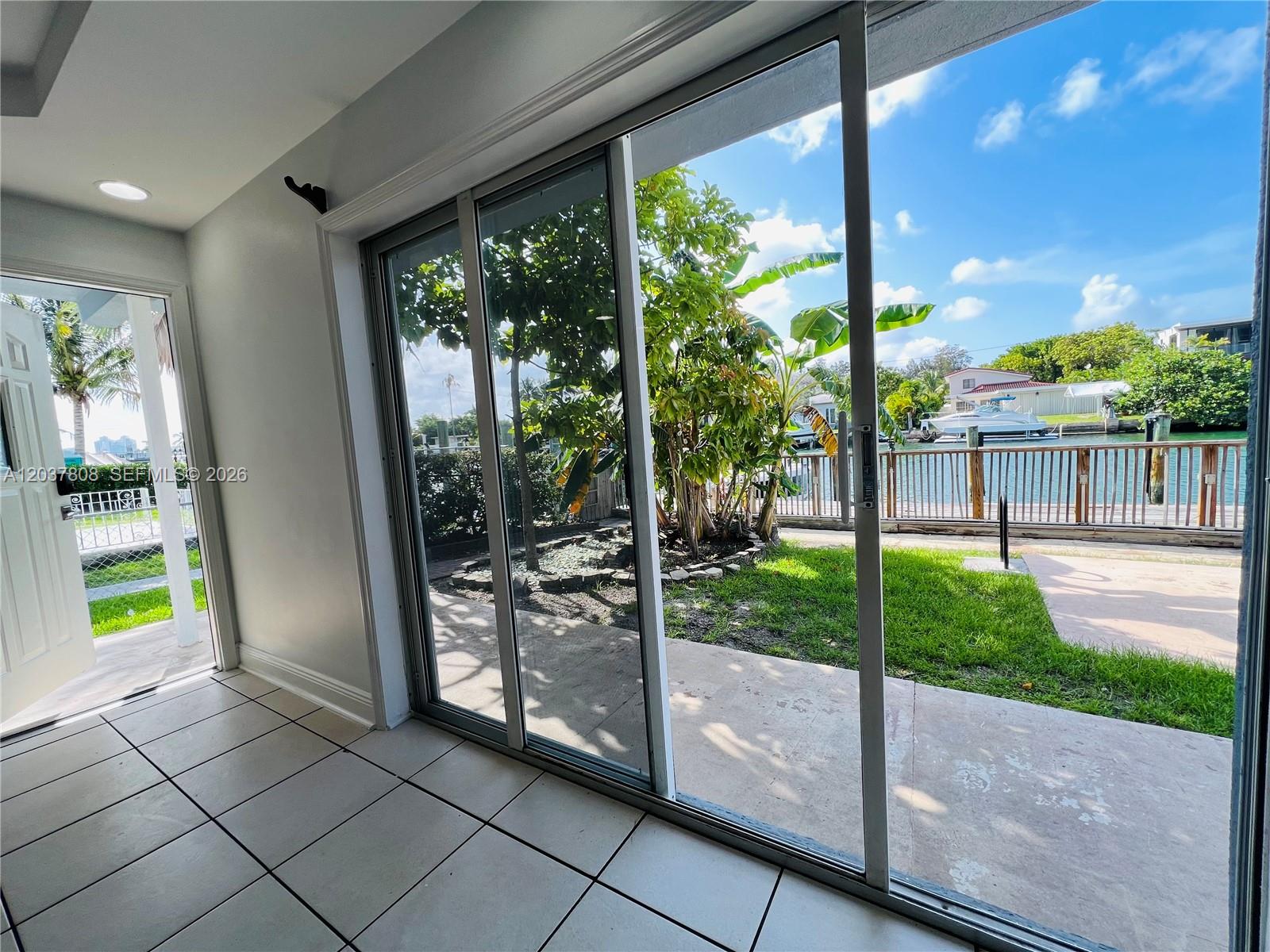 A room with tiled floors features sliding glass doors opening to a waterfront backyard — 2033 Calais Dr # 5, Miami Beach FL 33141, MIAMI BEACH, FL
