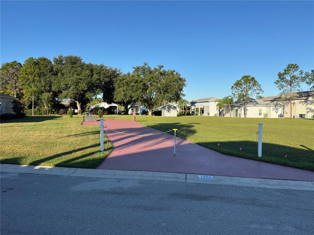A paved driveway leads to a large, grassy vacant lot in a residential neighborhood — 1052 CARAVAN LOOP, POLK CITY, FL