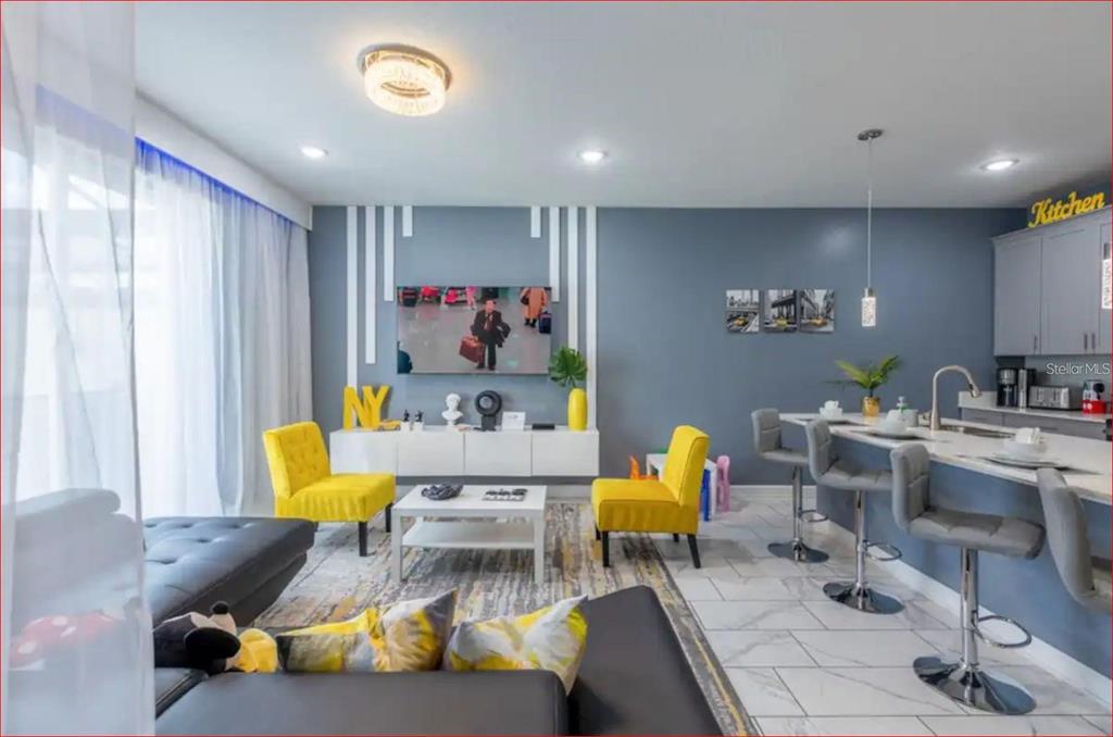 A modern open-concept living room and kitchen featuring gray walls, yellow accent chairs, and tile flooring — 1563 PLUNKER DRIVE, DAVENPORT, FL