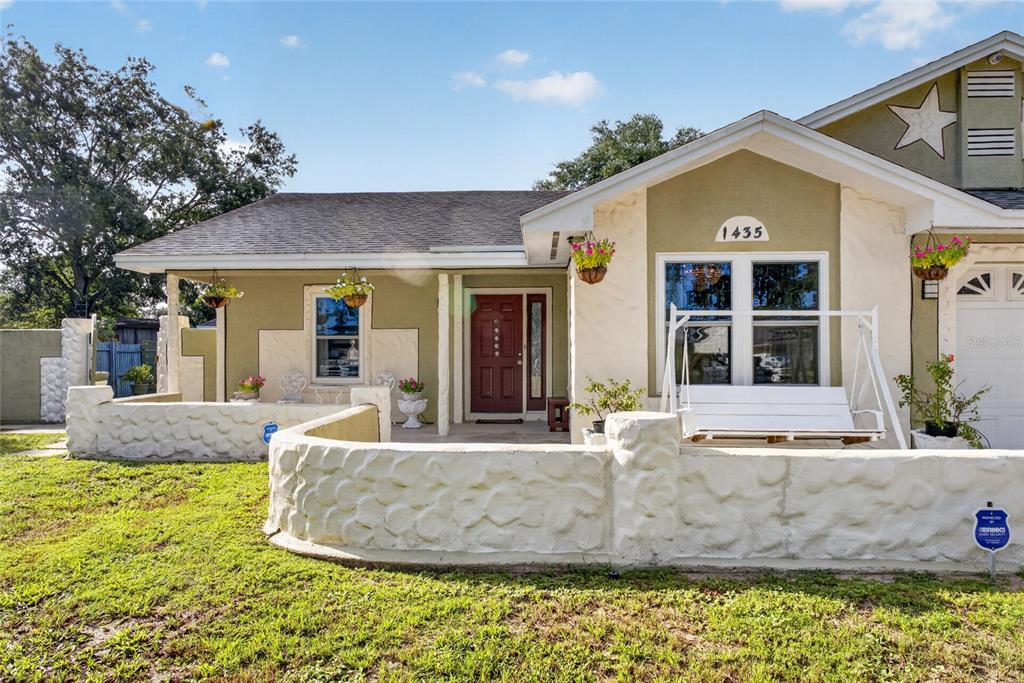 A single-story house with a white stone wall, a front porch swing, and a red door — 1435 LAMPLIGHTER WAY, ORLANDO, FL
