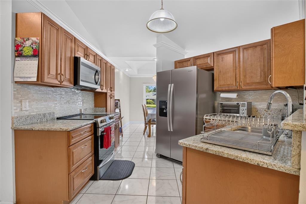 A kitchen with wood cabinets, granite countertops, stainless steel appliances, and white tile flooring — 1435 LAMPLIGHTER WAY, ORLANDO, FL