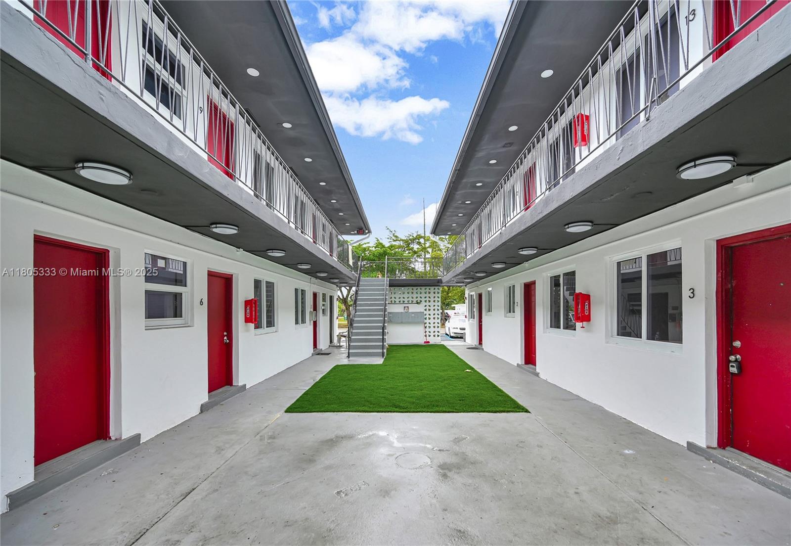 An exterior view of a two-story apartment complex with red doors and a central courtyard — 1265 Sharazad Blvd, Opa-Locka FL 33054, OPA-LOCKA, FL