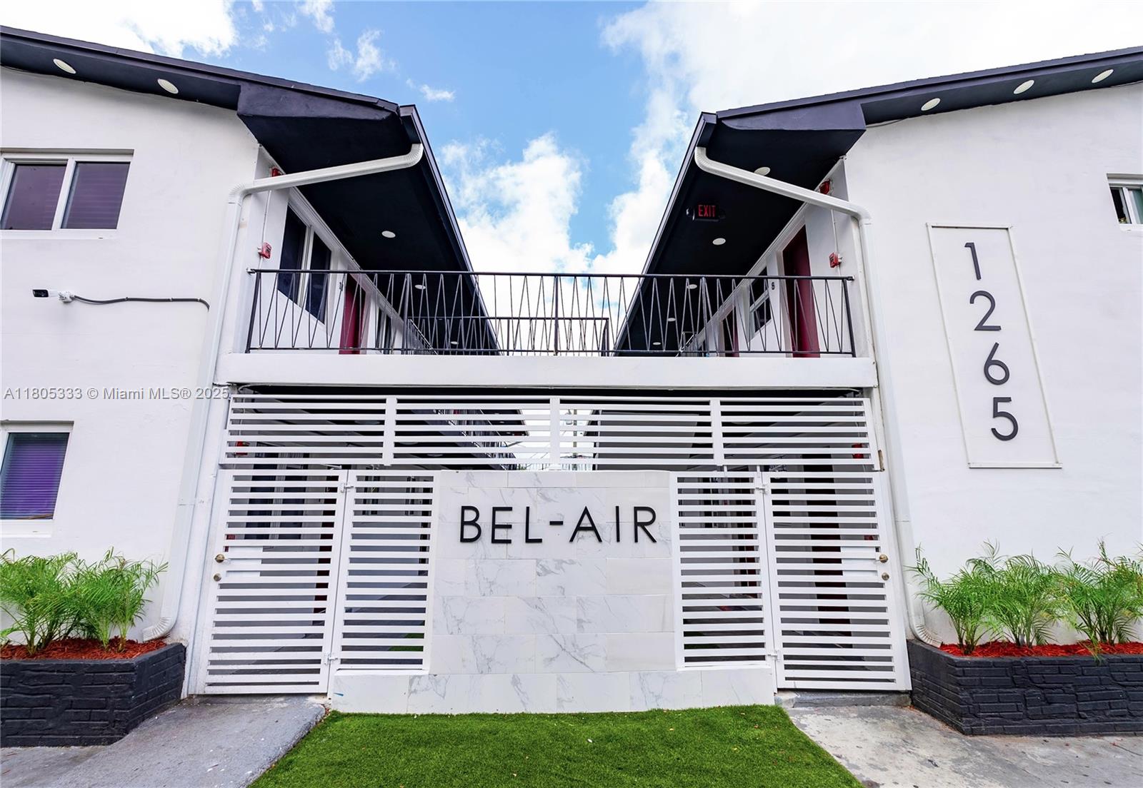 The exterior of a two-story apartment building features a white facade, gated entrance, and balcony — 1265 Sharazad Blvd, Opa-Locka FL 33054, OPA-LOCKA, FL