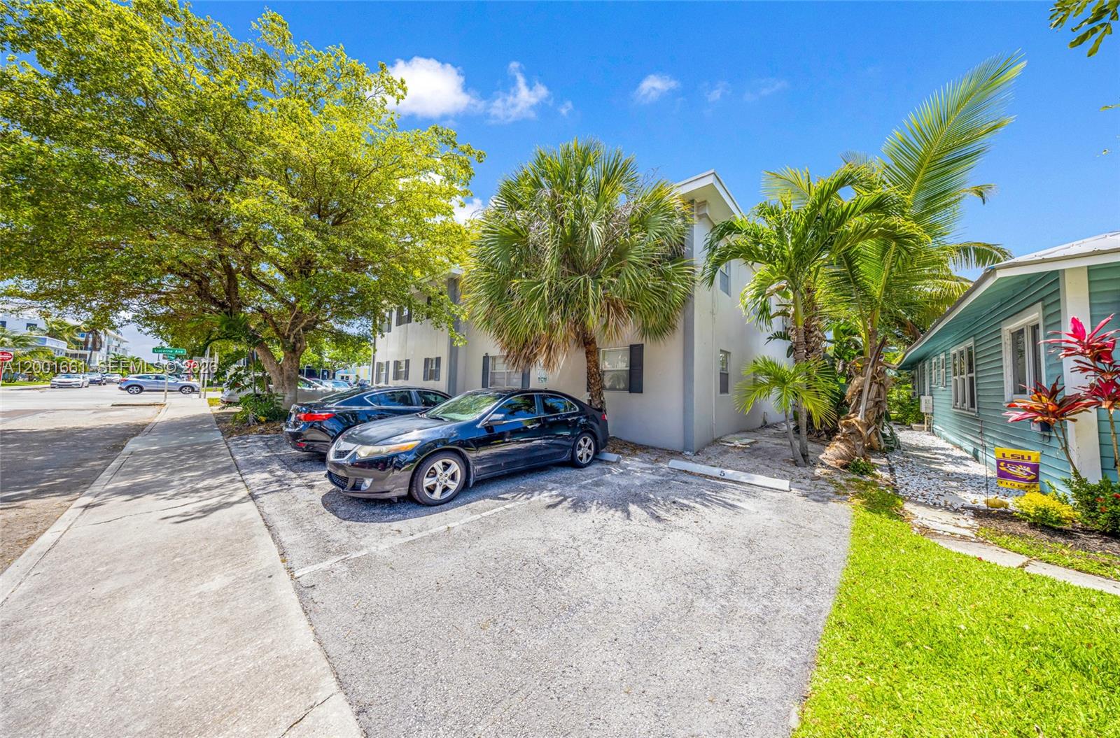 A two-story building with a parking area and palm trees sits beside a blue house — 202 Lucerne Ave # 14, Lake Worth FL 33460, LAKE WORTH, FL