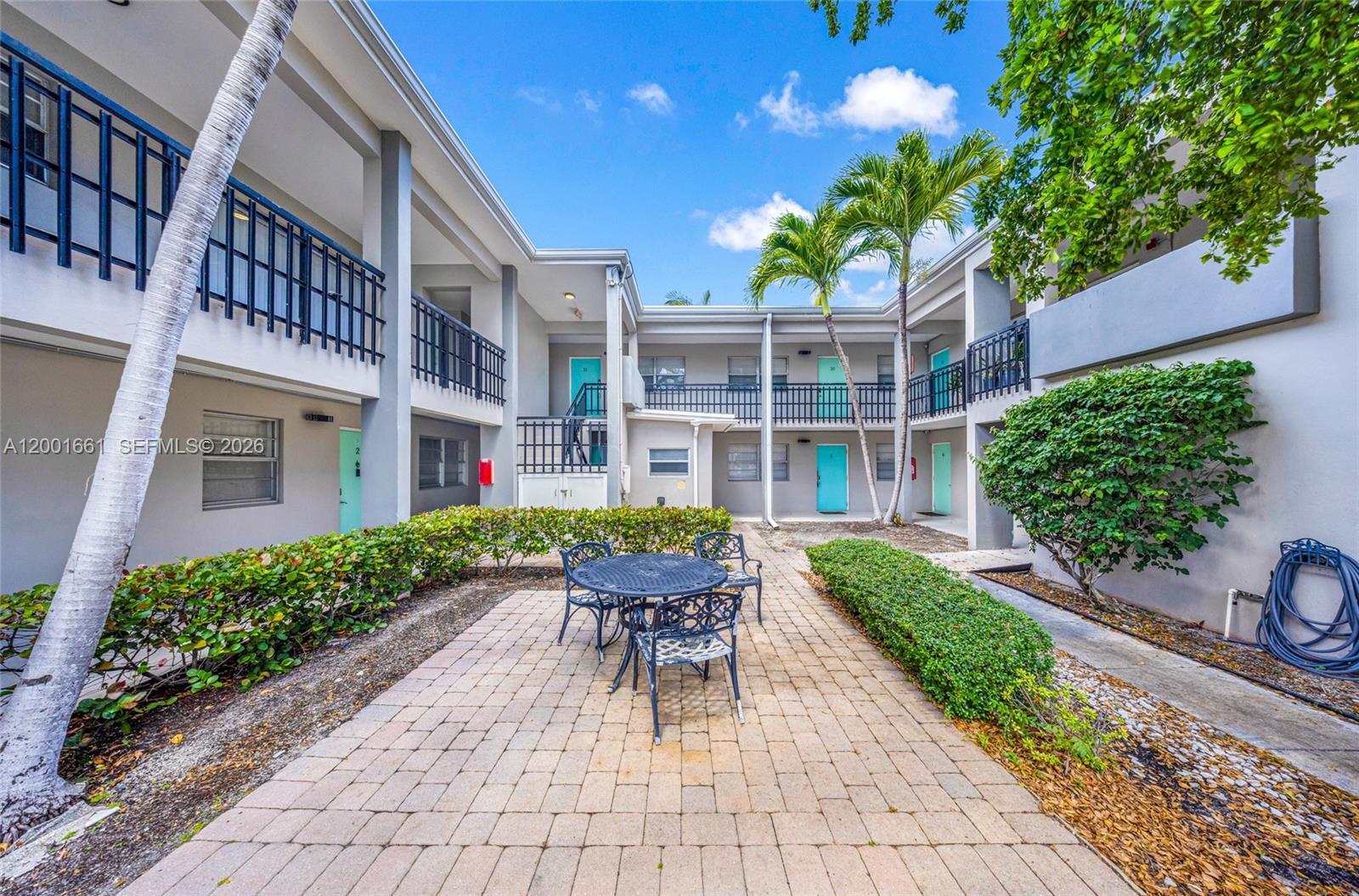 A paved courtyard with a table and chairs sits between two levels of apartment buildings — 202 Lucerne Ave # 14, Lake Worth FL 33460, LAKE WORTH, FL
