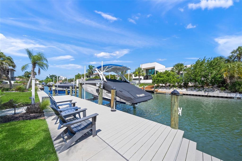 A boat on a lift sits at a dock with chairs beside a canal — 549 HALYARD LANE, LONGBOAT KEY, FL