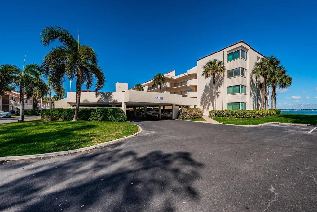 A multi-story apartment building with covered parking and palm trees under a clear blue sky — 5505 PUERTA DEL SOL BOULEVARD S UNIT 325, ST PETERSBURG, FL