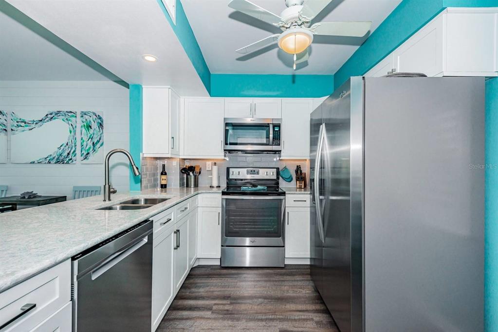 A kitchen features white cabinets, stainless steel appliances, granite countertops, and bright teal walls — 5505 PUERTA DEL SOL BOULEVARD S UNIT 325, ST PETERSBURG, FL