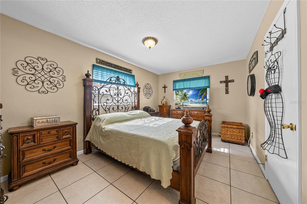 A bedroom features a wooden bed frame, tile flooring, and a dresser against a beige wall — 2208 GARDENIA WAY, LEHIGH ACRES, FL
