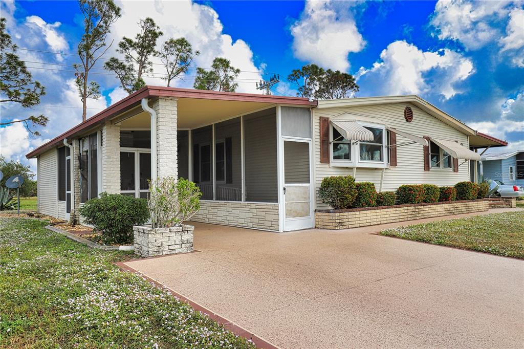 A single-story manufactured home with a screened-in porch, beige siding, and a concrete driveway — 666 ALVARADO, NORTH PORT, FL