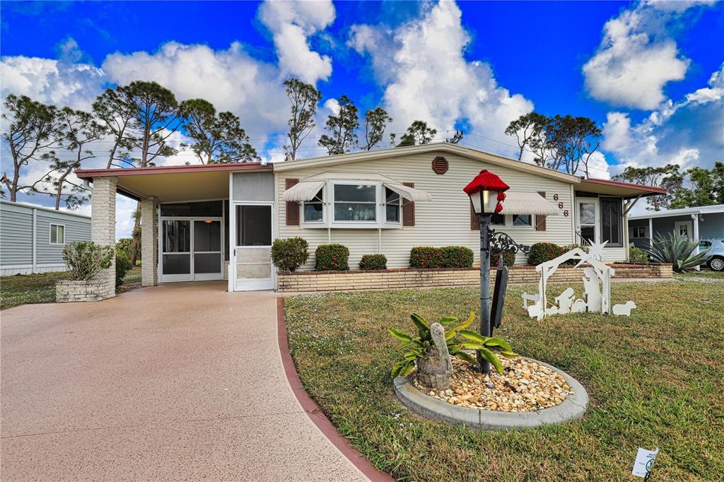 A single-story manufactured home features light siding, a covered carport, and a front lawn — 666 ALVARADO, NORTH PORT, FL