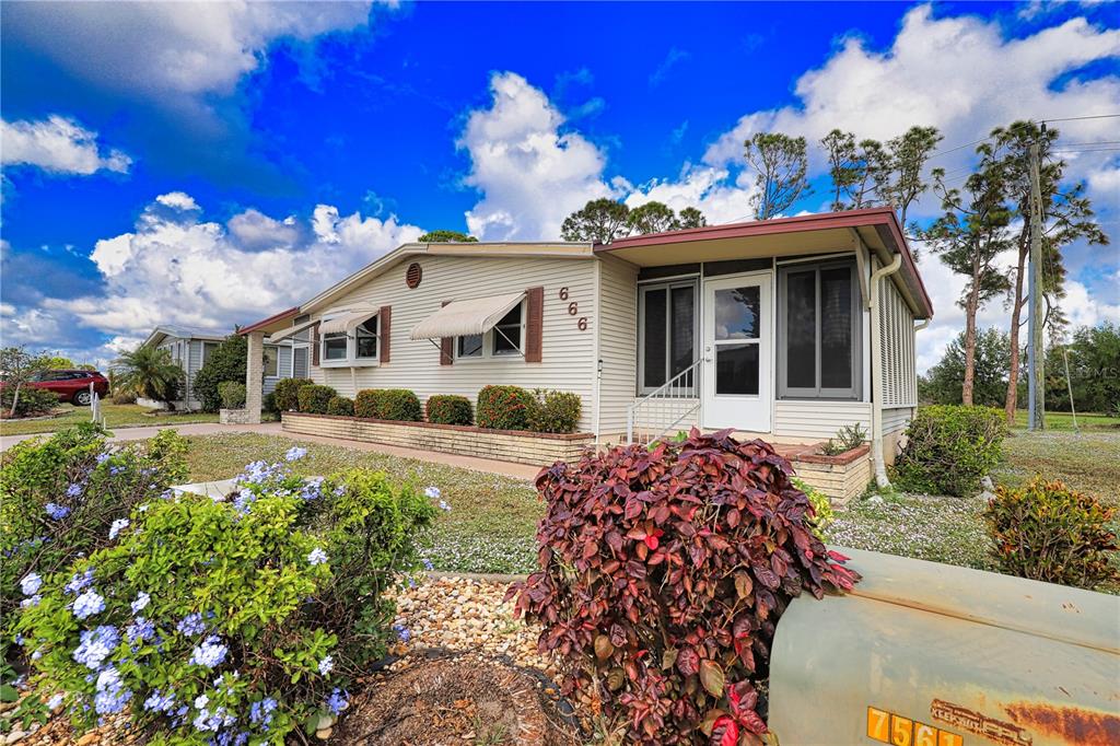 A single-story manufactured home with light siding, a screened porch, and a landscaped front yard — 666 ALVARADO, NORTH PORT, FL