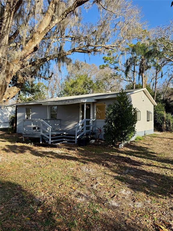 A single-story house with light gray siding and a wooden deck under large trees — 7700 VINE STREET, LAND O LAKES, FL